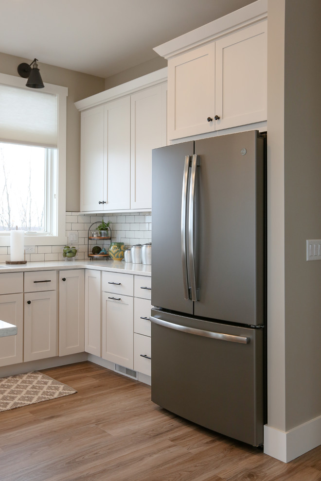 Inspiration for a large transitional u-shaped light wood floor and brown floor eat-in kitchen remodel with an undermount sink, recessed-panel cabinets, white cabinets, quartz countertops, white backsplash, subway tile backsplash, stainless steel appliances, an island and white countertops