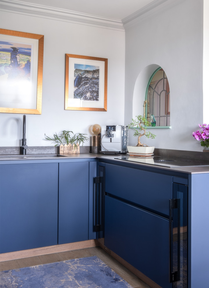Cette photo montre une petite cuisine éclectique en U fermée avec un évier posé, un placard à porte plane, des portes de placard bleues, un plan de travail en surface solide, un électroménager noir et un plan de travail gris.