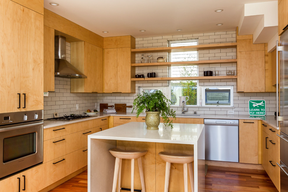 This is an example of a small contemporary u-shaped kitchen in Seattle with flat-panel cabinets, light wood cabinets, quartz benchtops, subway tile splashback, stainless steel appliances, with island, an undermount sink, white splashback, medium hardwood floors and brown floor.