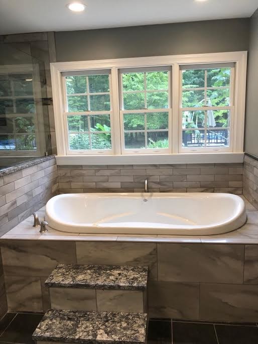 This is an example of a mid-sized transitional master bathroom in Richmond with recessed-panel cabinets, white cabinets, a drop-in tub, a corner shower, a two-piece toilet, beige tile, porcelain tile, green walls, porcelain floors, an undermount sink, granite benchtops, black floor, a hinged shower door and black benchtops.