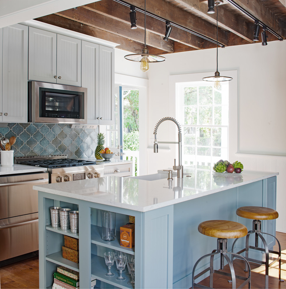 Photo of a country galley kitchen in Atlanta with a farmhouse sink, beaded inset cabinets, grey cabinets, quartz benchtops, blue splashback, terra-cotta splashback, stainless steel appliances, medium hardwood floors, with island and brown floor.