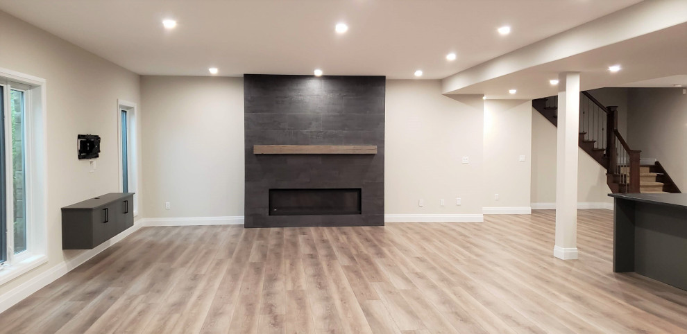 Large transitional walk-out vinyl floor basement photo with a bar and a tile fireplace