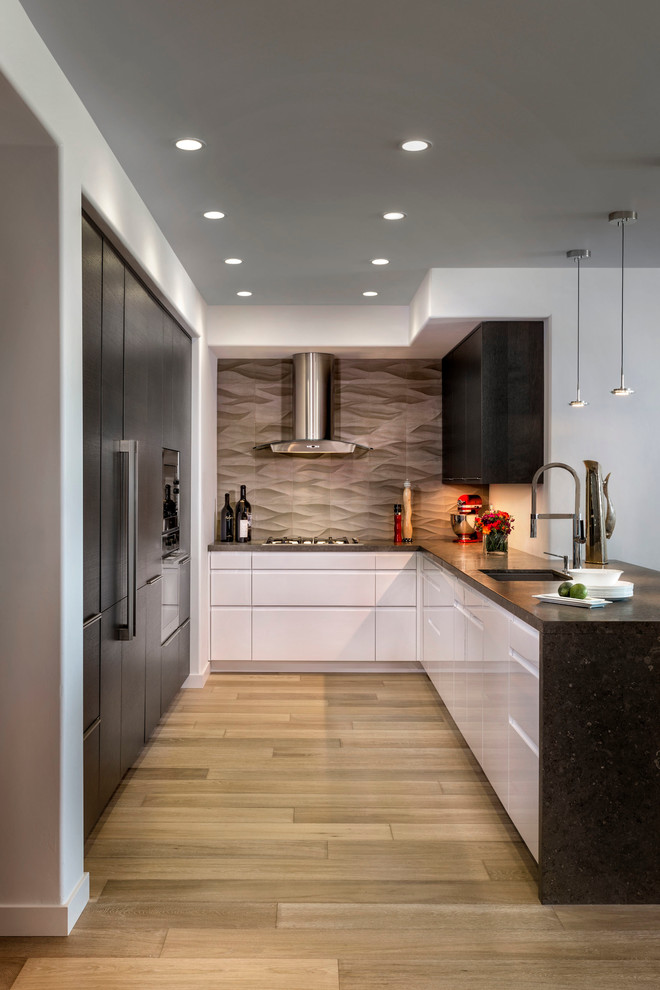 This is an example of a contemporary u-shaped kitchen in Orange County with flat-panel cabinets, white cabinets, grey splashback, light hardwood floors, a peninsula and limestone splashback.
