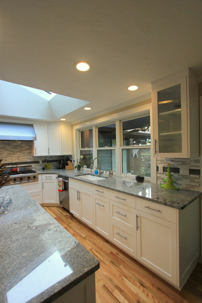 Example of a large transitional u-shaped light wood floor open concept kitchen design with an undermount sink, shaker cabinets, white cabinets, granite countertops, multicolored backsplash, mosaic tile backsplash, stainless steel appliances and an island