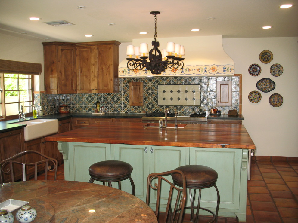 Inspiration for a large l-shaped eat-in kitchen in Phoenix with a farmhouse sink, recessed-panel cabinets, distressed cabinets, wood benchtops, multi-coloured splashback, terra-cotta splashback, panelled appliances, with island and terra-cotta floors.