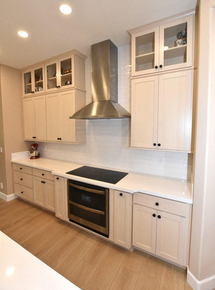 Example of a large transitional l-shaped vinyl floor and beige floor kitchen design with an undermount sink, shaker cabinets, light wood cabinets, solid surface countertops, white backsplash, porcelain backsplash, stainless steel appliances, an island and white countertops