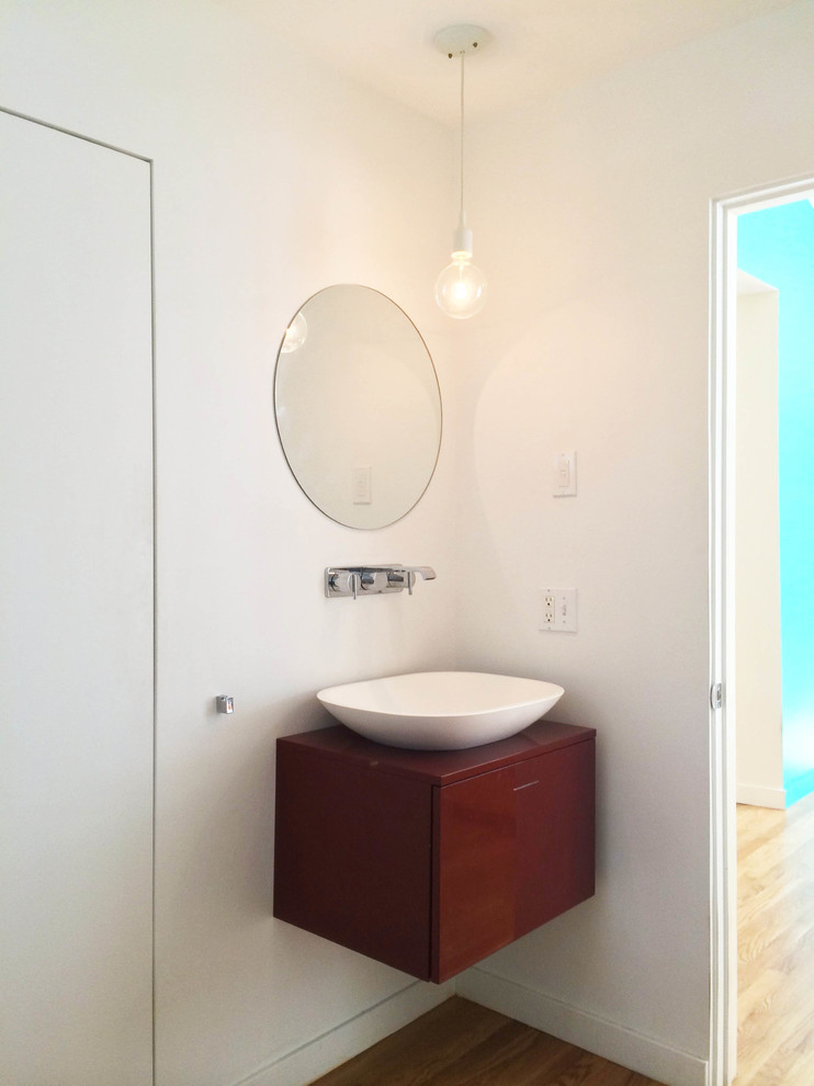 Small midcentury master bathroom in New York with a vessel sink, flat-panel cabinets, red cabinets, a freestanding tub, a wall-mount toilet, white walls and light hardwood floors.