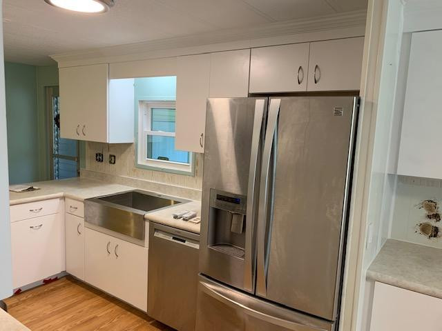 Kitchen pantry - large u-shaped kitchen pantry idea with a farmhouse sink, flat-panel cabinets, white cabinets, laminate countertops, white backsplash, stainless steel appliances, a peninsula and white countertops
