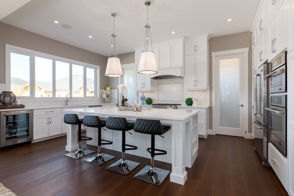 Inspiration for a transitional u-shaped dark wood floor kitchen remodel in Calgary with shaker cabinets, white cabinets, white backsplash, subway tile backsplash, stainless steel appliances and an island