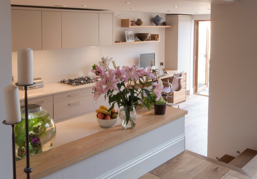 Mid-sized contemporary galley separate kitchen in Other with a drop-in sink, flat-panel cabinets, beige cabinets, quartz benchtops, white splashback, glass sheet splashback, stainless steel appliances and medium hardwood floors.