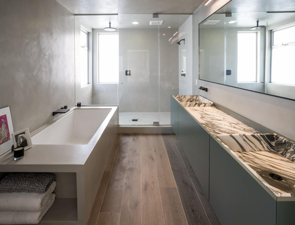This is an example of a mid-sized modern master bathroom in Los Angeles with flat-panel cabinets, grey cabinets, an alcove shower, a one-piece toilet, grey walls, medium hardwood floors, an integrated sink, marble benchtops, a hinged shower door and white benchtops.