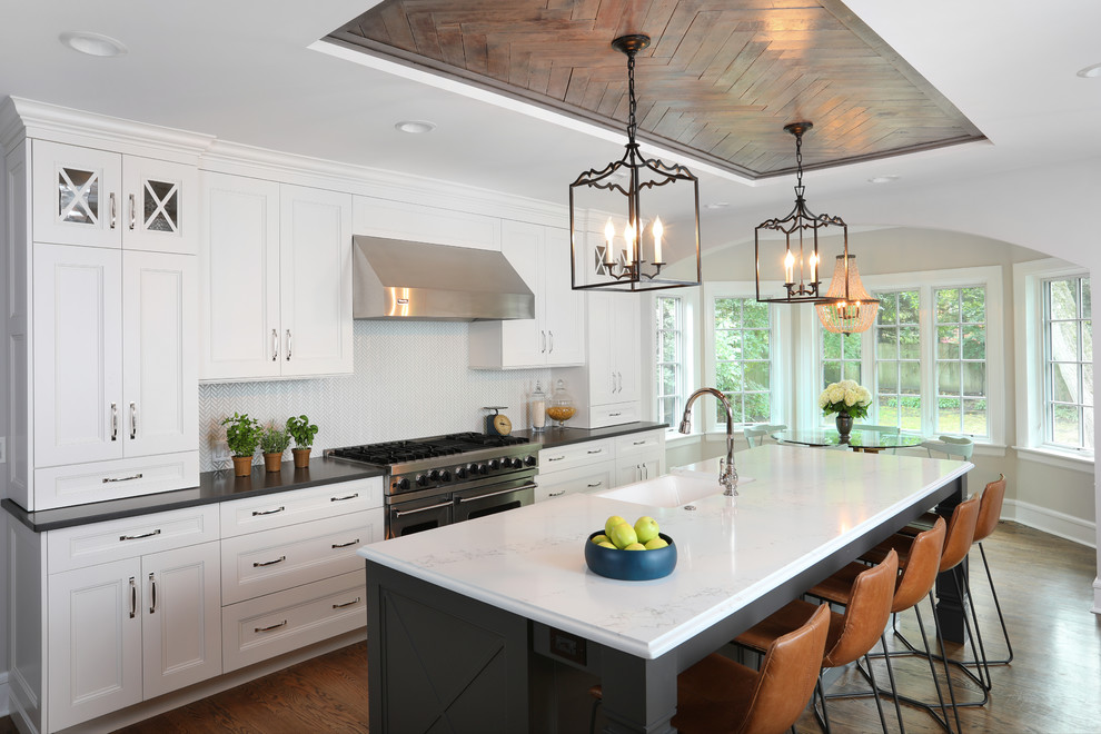 This is an example of a large eclectic l-shaped open plan kitchen in Chicago with white cabinets, quartz benchtops, white splashback, ceramic splashback, stainless steel appliances, medium hardwood floors, with island, brown floor, black benchtop, recessed-panel cabinets and a farmhouse sink.