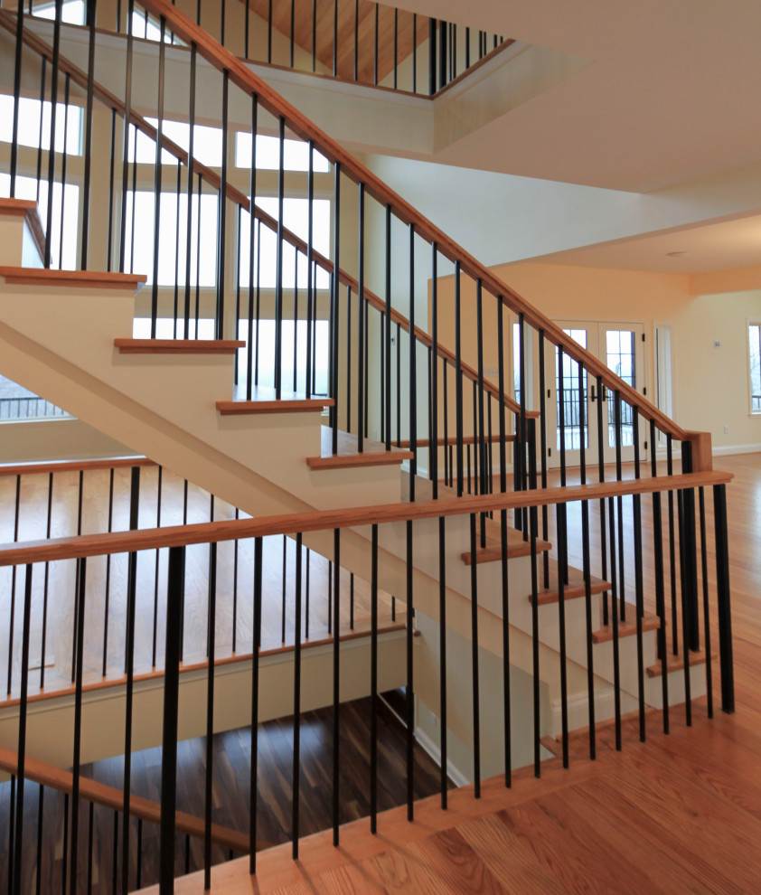 This is an example of a large transitional wood floating staircase in DC Metro with wood risers, mixed railing and planked wall panelling.