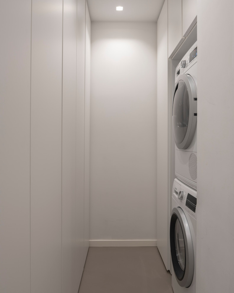 Photo of a mid-sized modern u-shaped utility room in Milan with flat-panel cabinets, white cabinets, white walls, a stacked washer and dryer, grey floor and recessed.