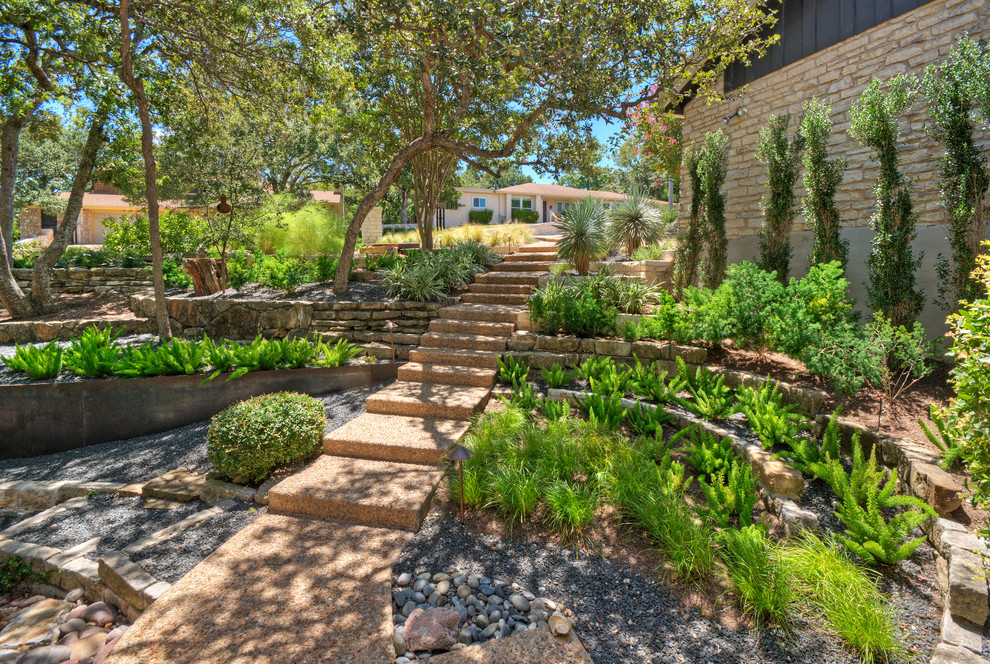 Inspiration for a large contemporary front yard shaded xeriscape for spring in Austin with a retaining wall and gravel.