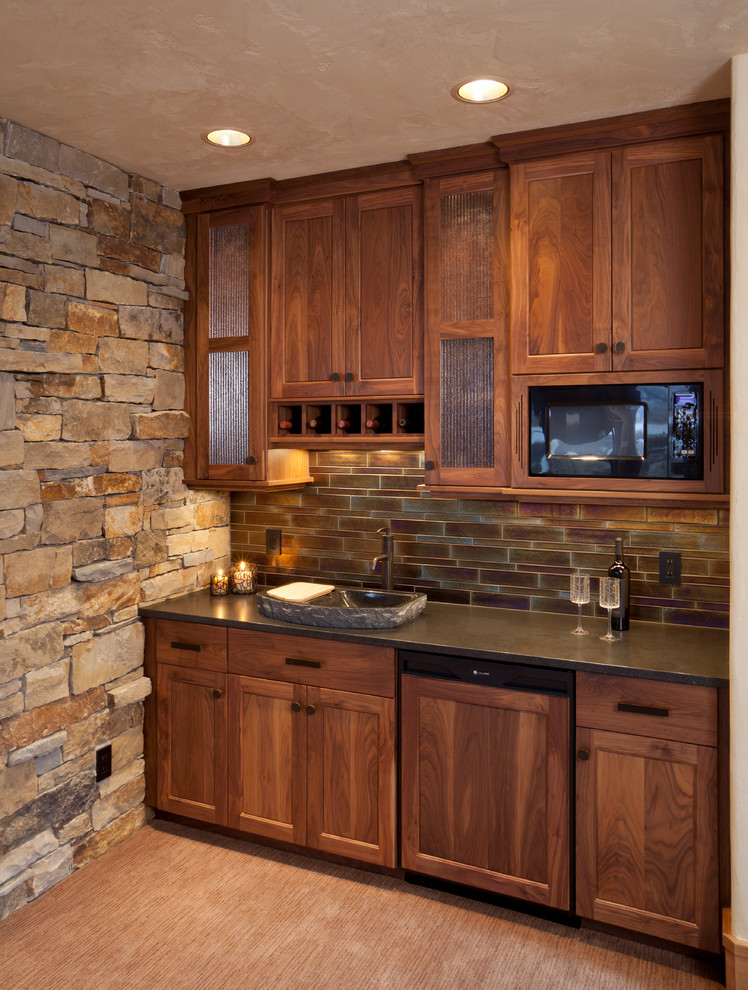 Photo of a country single-wall wet bar in Denver with a drop-in sink, flat-panel cabinets, medium wood cabinets, granite benchtops, multi-coloured splashback, glass tile splashback, carpet, beige floor and black benchtop.
