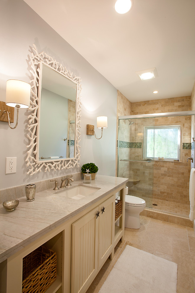 This is an example of a mid-sized beach style 3/4 bathroom in Miami with shaker cabinets, beige cabinets, an alcove shower, a two-piece toilet, beige tile, marble, grey walls, marble floors, a drop-in sink, quartzite benchtops, beige floor and a sliding shower screen.