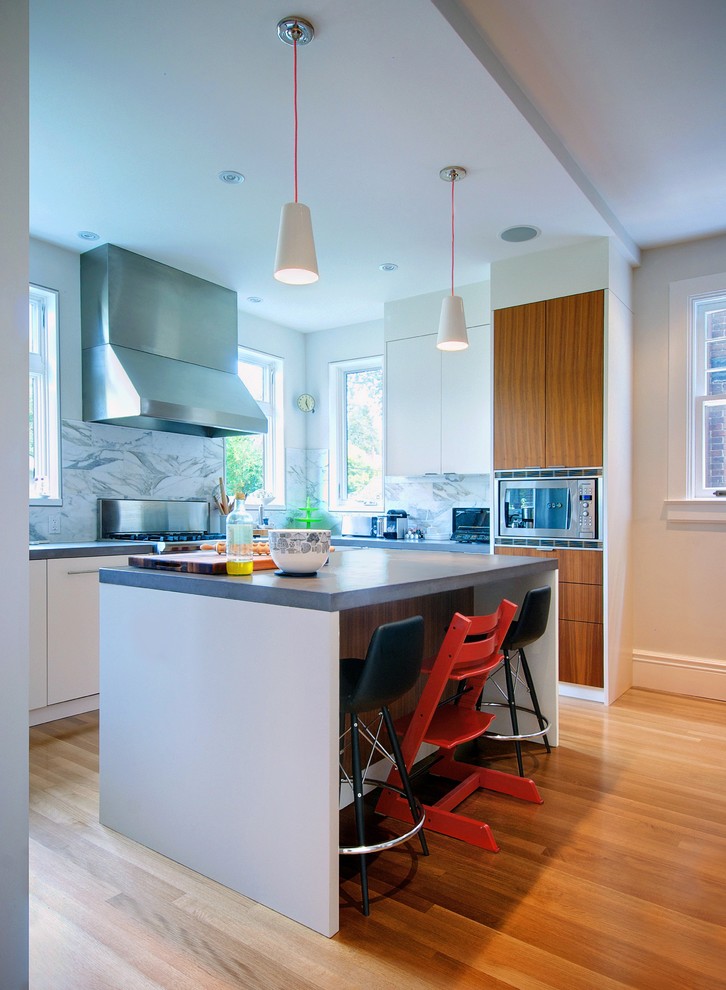 Design ideas for a mid-sized modern l-shaped eat-in kitchen in Toronto with concrete benchtops, flat-panel cabinets, multi-coloured splashback, marble splashback, stainless steel appliances, medium hardwood floors, with island, brown floor and grey benchtop.