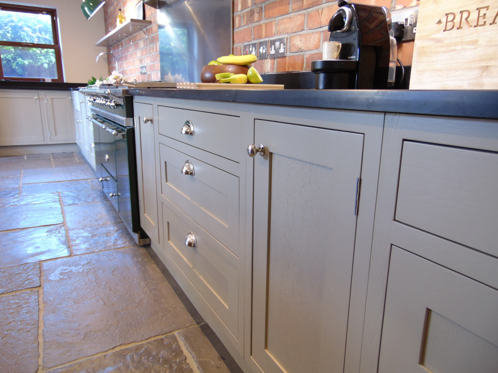 Photo of a mid-sized transitional l-shaped eat-in kitchen with a farmhouse sink, shaker cabinets, grey cabinets, coloured appliances, limestone floors, no island, grey floor and black benchtop.