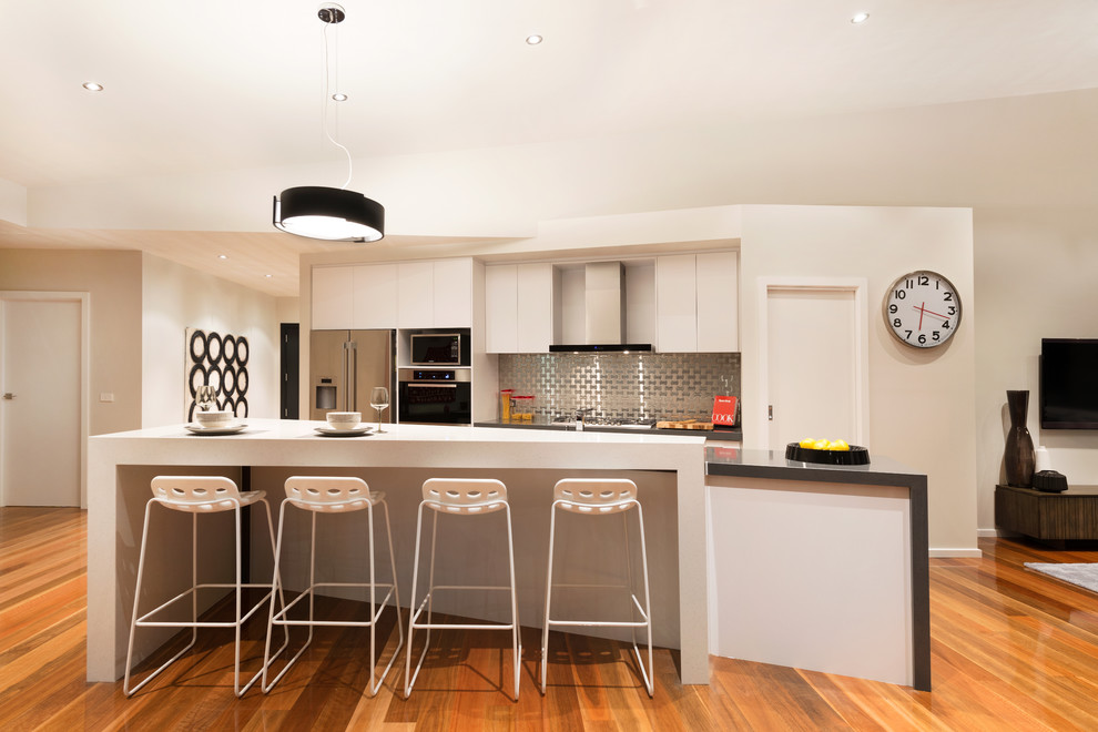 Photo of a contemporary kitchen in Melbourne with flat-panel cabinets, white cabinets, metallic splashback and stainless steel appliances.
