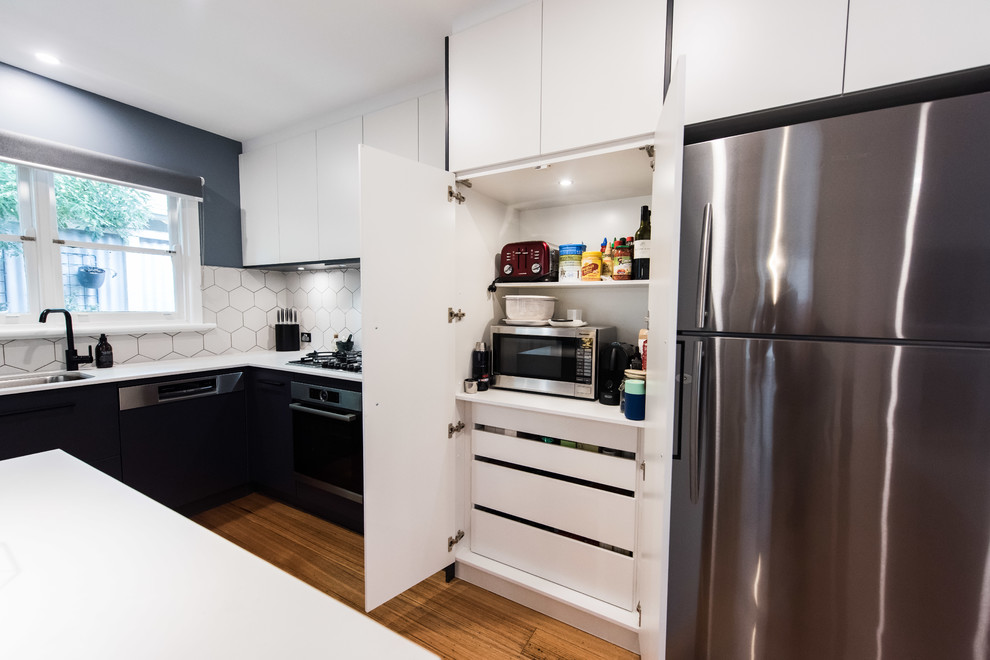 Mid-sized contemporary l-shaped open plan kitchen in Melbourne with an undermount sink, flat-panel cabinets, black cabinets, quartz benchtops, white splashback, ceramic splashback, stainless steel appliances, light hardwood floors, with island and brown floor.