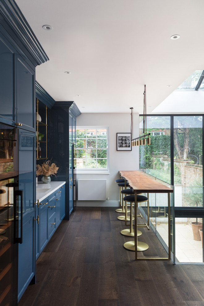 Design ideas for a large contemporary single-wall wet bar in London with a built-in sink, shaker cabinets, blue cabinets, quartz worktops, mirror splashback, dark hardwood flooring and brown floors.