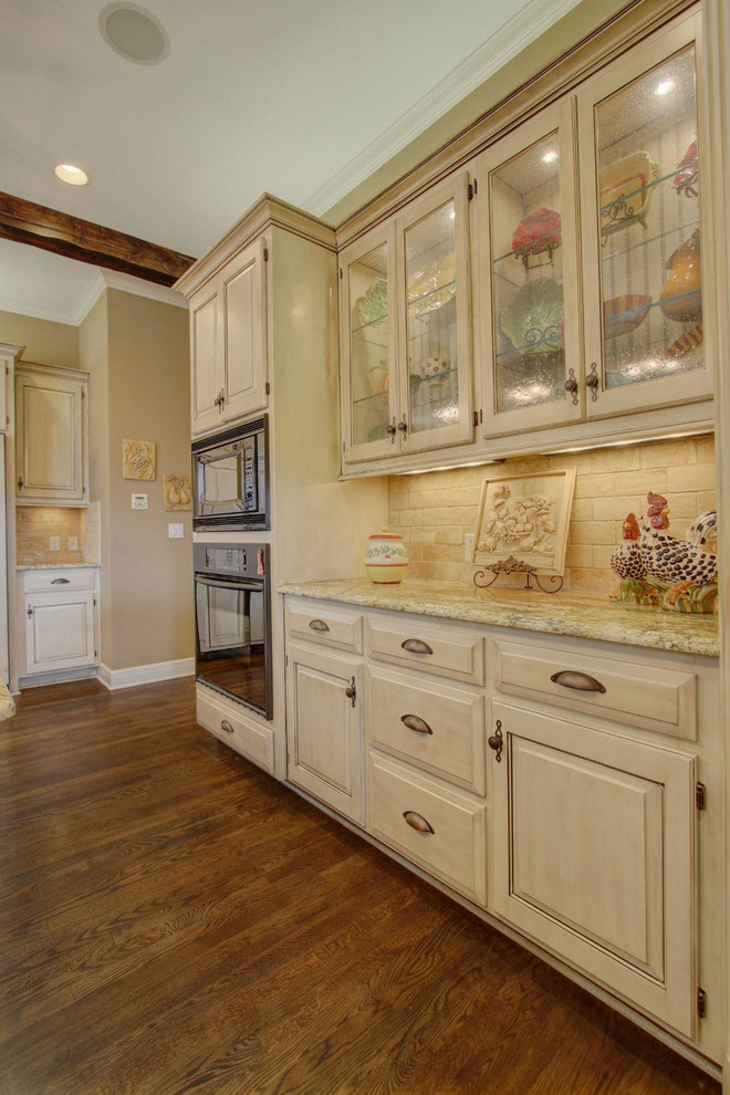 This is an example of a large u-shaped eat-in kitchen in Kansas City with a double-bowl sink, raised-panel cabinets, distressed cabinets, granite benchtops, beige splashback, stone tile splashback, panelled appliances, dark hardwood floors and with island.