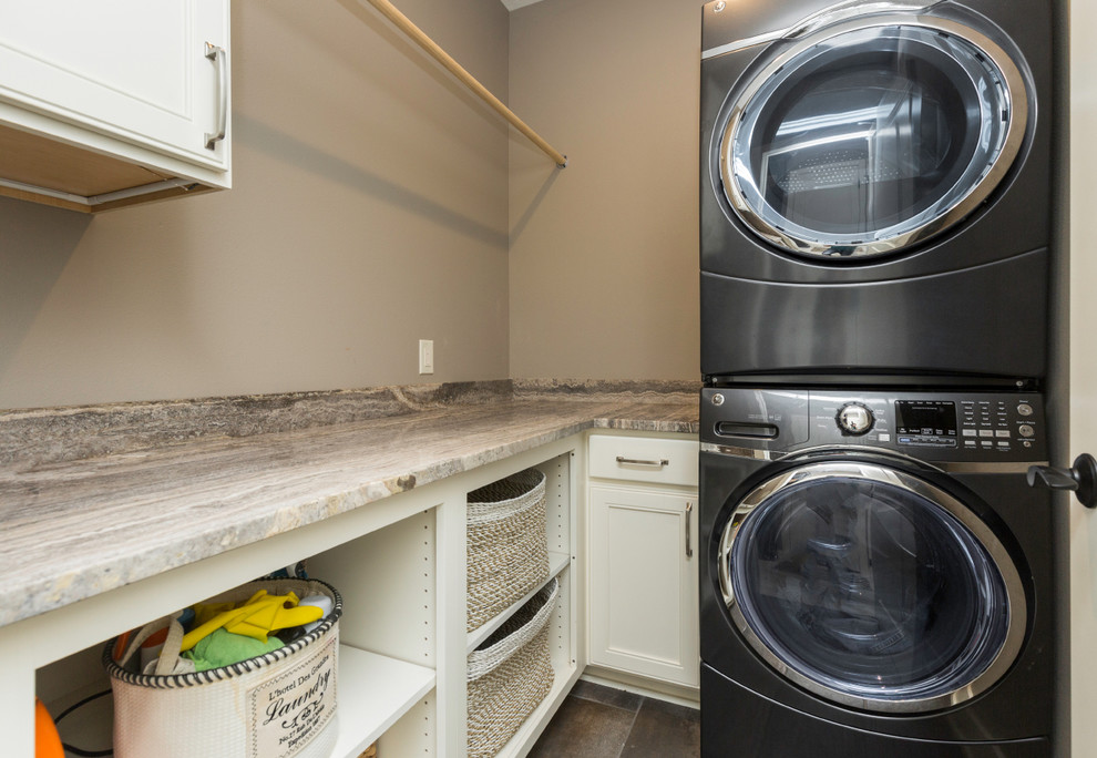 Small traditional l-shaped dedicated laundry room in Other with beaded inset cabinets, white cabinets, granite benchtops, grey walls, porcelain floors, a stacked washer and dryer, brown floor and brown benchtop.