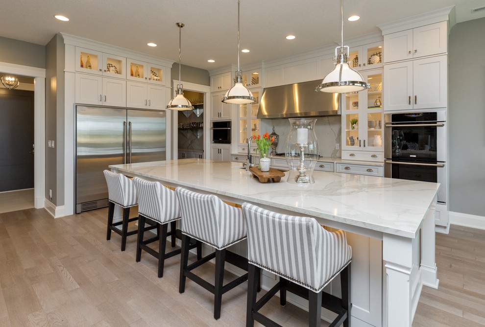 Eat-in kitchen - large transitional l-shaped porcelain tile eat-in kitchen idea with a farmhouse sink, shaker cabinets, white cabinets, marble countertops, stainless steel appliances and an island