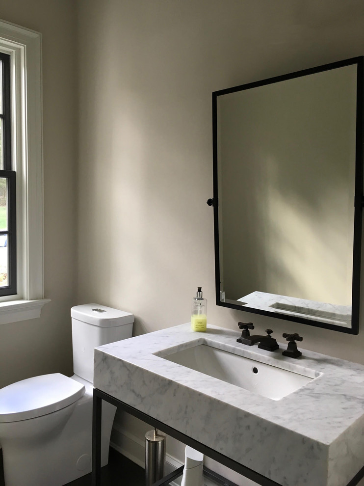 This is an example of a mid-sized contemporary powder room in New York with a two-piece toilet, dark hardwood floors, beige walls, an undermount sink, marble benchtops, brown floor and white benchtops.