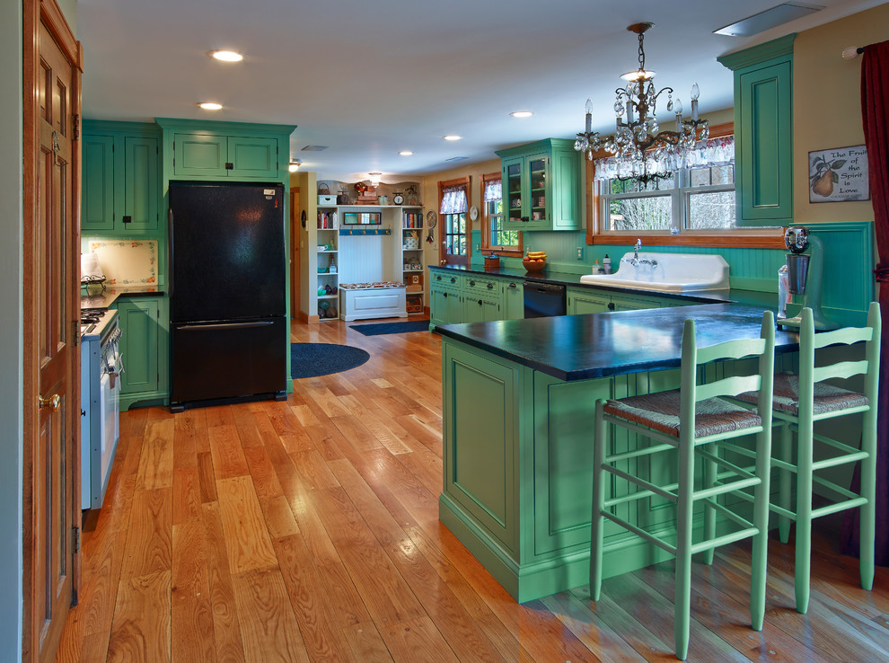 This is an example of a mid-sized eclectic l-shaped eat-in kitchen in Providence with a drop-in sink, beaded inset cabinets, green cabinets, soapstone benchtops, green splashback, timber splashback, black appliances, medium hardwood floors and no island.