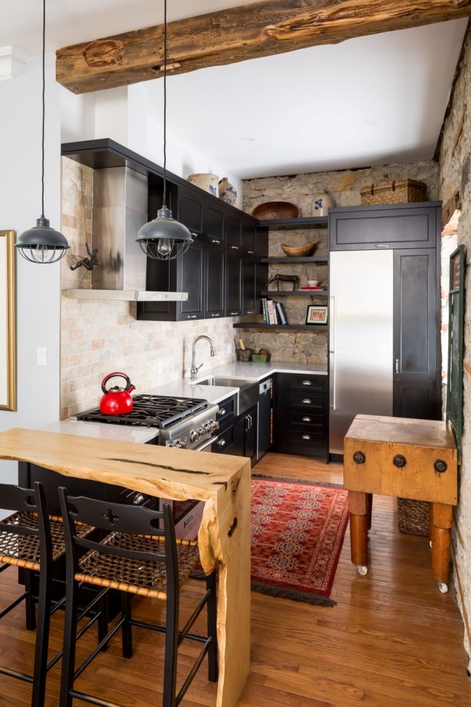 Inspiration for a country l-shaped kitchen in Toronto with a farmhouse sink, shaker cabinets, black cabinets, beige splashback, stone tile splashback, stainless steel appliances, medium hardwood floors and brown floor.