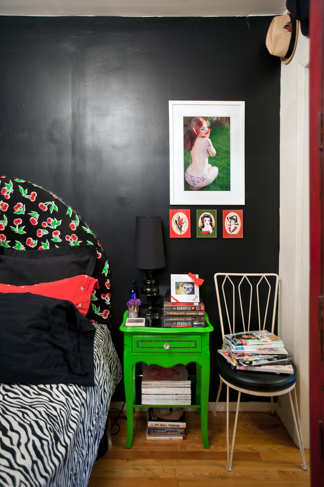 This is an example of a small eclectic bedroom in New York with black walls and medium hardwood floors.