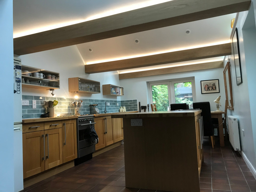 This is an example of a mid-sized contemporary l-shaped eat-in kitchen in Hampshire with with island, an integrated sink, wood benchtops, grey splashback, stone tile splashback, white appliances, slate floors, grey floor and exposed beam.