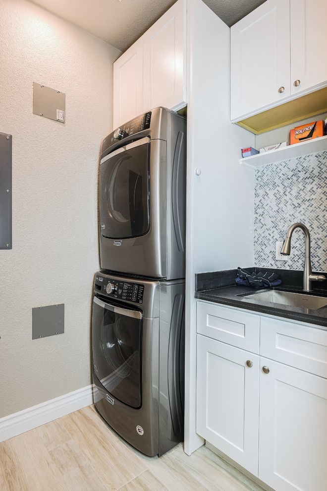 Small transitional u-shaped utility room in San Francisco with an undermount sink, shaker cabinets, white cabinets, quartz benchtops, grey walls, porcelain floors, a stacked washer and dryer and beige floor.