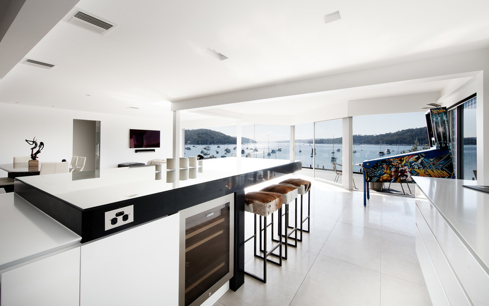 Photo of a mid-sized contemporary galley kitchen in Sydney with a double-bowl sink, recessed-panel cabinets, white cabinets, quartz benchtops, white splashback, glass sheet splashback, stainless steel appliances, porcelain floors, with island, grey floor and black benchtop.