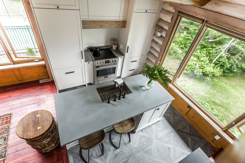 Large country u-shaped eat-in kitchen in Montreal with an undermount sink, shaker cabinets, concrete benchtops, white splashback, panelled appliances, porcelain floors, with island, grey floor, grey benchtop, white cabinets and ceramic splashback.