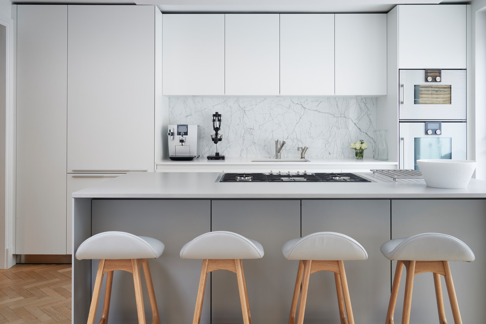 Photo of a mid-sized contemporary l-shaped eat-in kitchen in London with flat-panel cabinets, white cabinets, laminate benchtops, white splashback, marble splashback, light hardwood floors, with island, beige floor, grey benchtop, an undermount sink and white appliances.