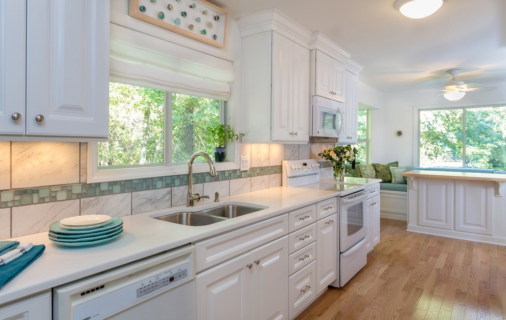 Enclosed kitchen - transitional galley enclosed kitchen idea in Raleigh with an undermount sink, raised-panel cabinets, white cabinets, quartz countertops, gray backsplash, porcelain backsplash and white appliances