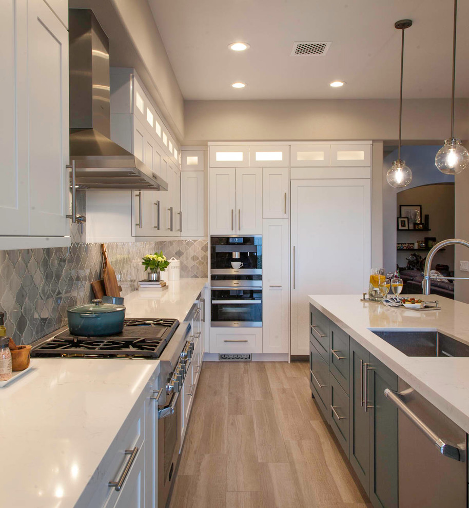 This is an example of a large transitional u-shaped eat-in kitchen in San Diego with an undermount sink, recessed-panel cabinets, white cabinets, quartz benchtops, grey splashback, glass tile splashback, stainless steel appliances, light hardwood floors, with island, beige floor and white benchtop.