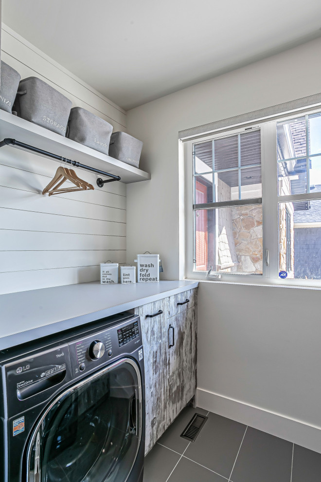 This is an example of a small industrial u-shaped dedicated laundry room in Calgary with flat-panel cabinets, distressed cabinets, laminate benchtops, white splashback, shiplap splashback, ceramic floors, grey floor and grey benchtop.