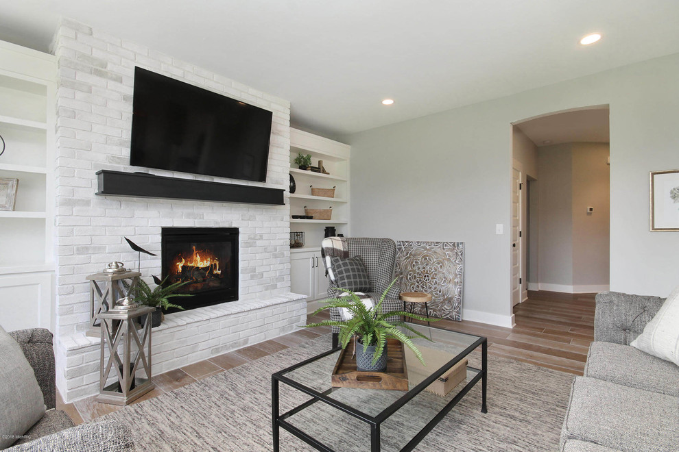 Photo of a mid-sized contemporary enclosed family room in Grand Rapids with grey walls, medium hardwood floors, a standard fireplace, a brick fireplace surround, a wall-mounted tv and brown floor.
