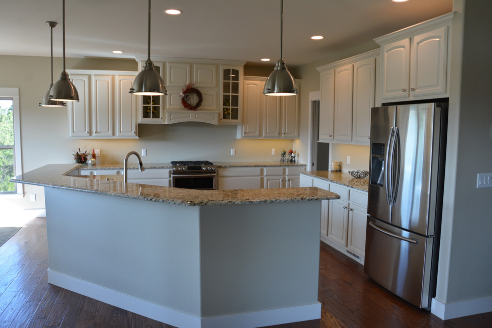 Example of a large transitional l-shaped medium tone wood floor and brown floor kitchen design with raised-panel cabinets, white cabinets, granite countertops, stainless steel appliances and an island