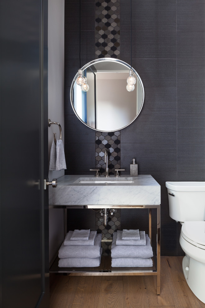 This is an example of a small eclectic powder room in Denver with a two-piece toilet, multi-coloured tile, grey walls, medium hardwood floors, a drop-in sink, granite benchtops, beige floor and white benchtops.