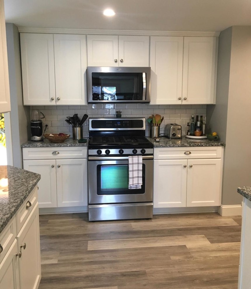 This is an example of a small transitional galley separate kitchen in New York with an undermount sink, shaker cabinets, white cabinets, granite benchtops, white splashback, subway tile splashback, stainless steel appliances, laminate floors, grey floor and grey benchtop.