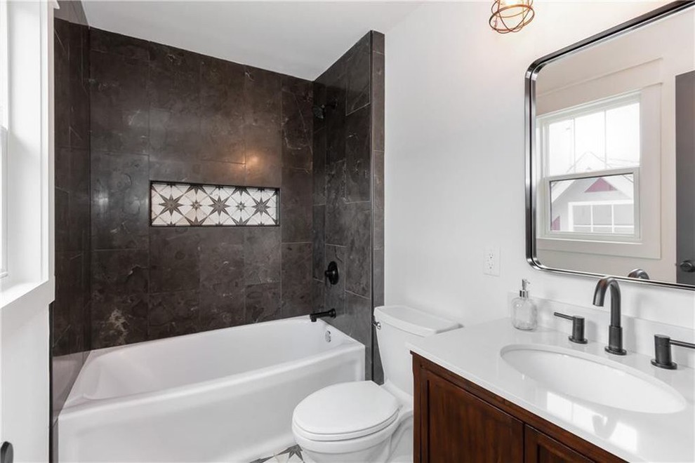 This is an example of a mid-sized transitional 3/4 bathroom in Indianapolis with recessed-panel cabinets, brown cabinets, an alcove tub, a shower/bathtub combo, a two-piece toilet, gray tile, porcelain tile, white walls, ceramic floors, an undermount sink, quartzite benchtops, multi-coloured floor, a shower curtain and white benchtops.