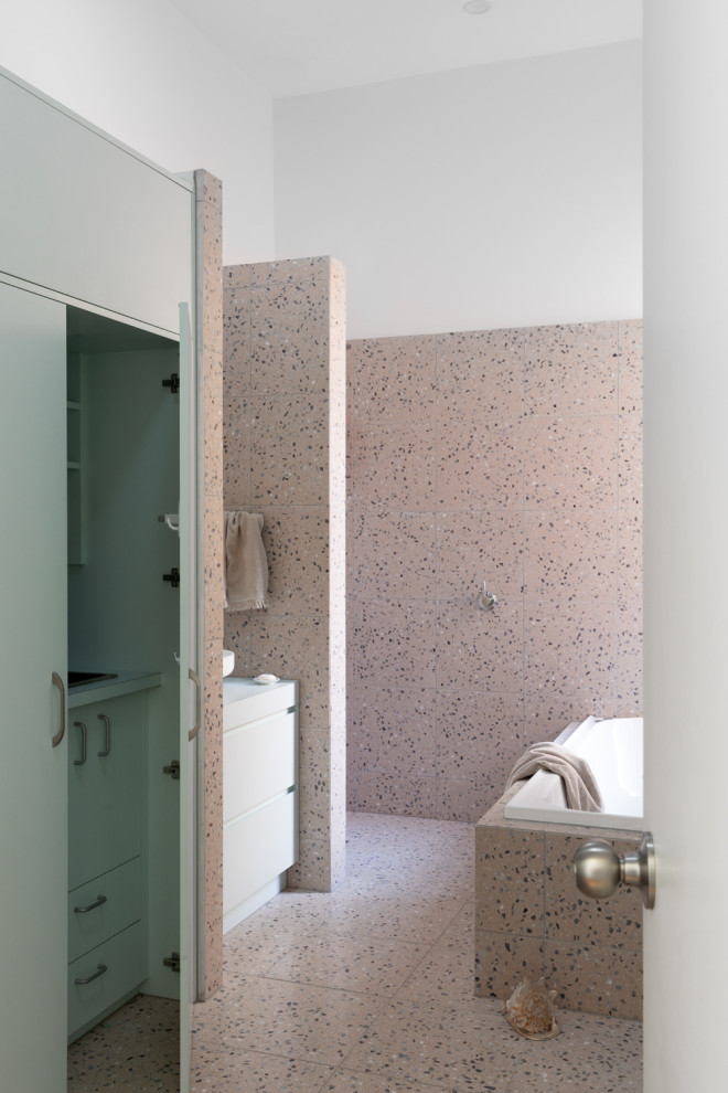 This is an example of a medium sized bohemian ensuite bathroom in Melbourne with flat-panel cabinets, green cabinets, a built-in bath, a walk-in shower, a two-piece toilet, pink tiles, stone tiles, pink walls, terrazzo flooring, a vessel sink, laminate worktops, pink floors, an open shower, green worktops, a laundry area, a single sink and a built in vanity unit.