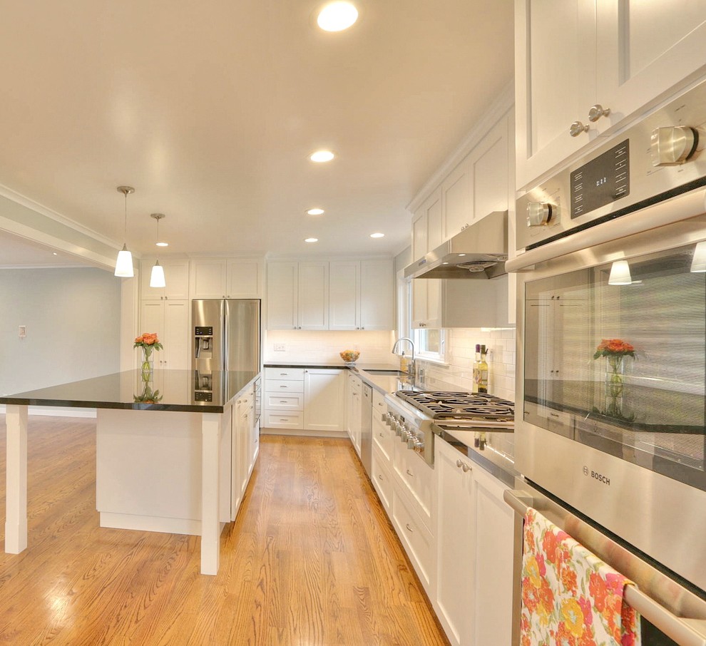 Photo of a contemporary l-shaped open plan kitchen in San Francisco with an undermount sink, shaker cabinets, white cabinets, granite benchtops, white splashback, ceramic splashback, stainless steel appliances, medium hardwood floors and with island.