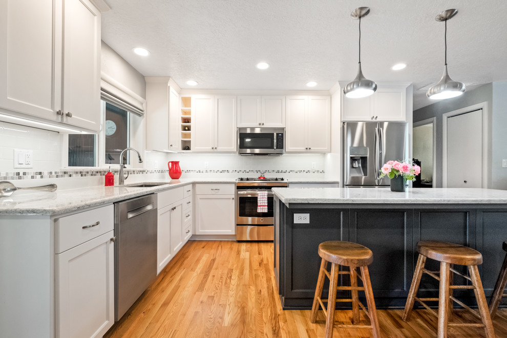 Inspiration for a large transitional l-shaped medium tone wood floor and brown floor eat-in kitchen remodel with a drop-in sink, recessed-panel cabinets, white cabinets, quartzite countertops, white backsplash, ceramic backsplash, stainless steel appliances, an island and white countertops