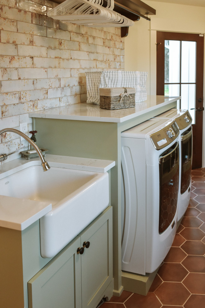 Mid-sized country single-wall dedicated laundry room in Portland with a farmhouse sink, shaker cabinets, green cabinets, quartz benchtops, white walls, terra-cotta floors, a side-by-side washer and dryer, brown floor and white benchtop.